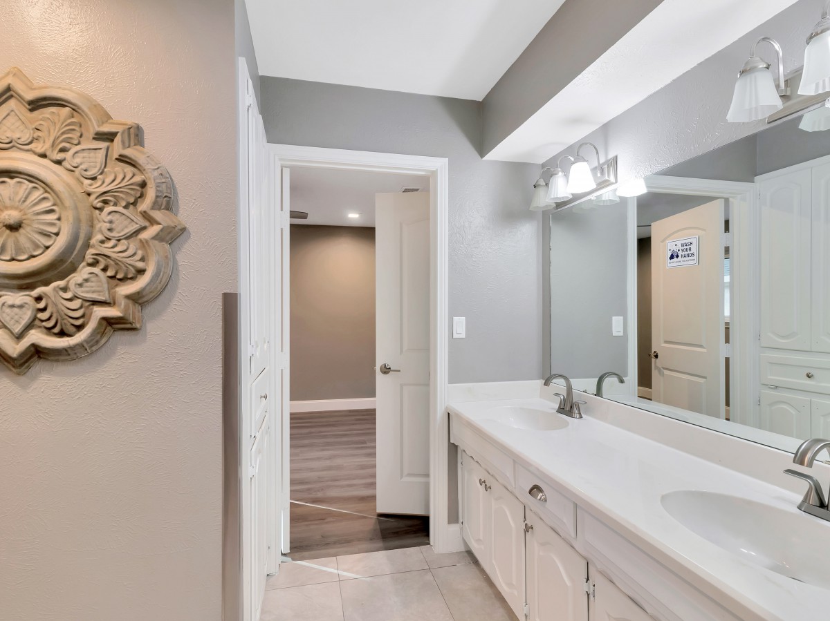 A modern bathroom with a large mirror and dual sink setup, featuring sleek lighting and decorative wall art.