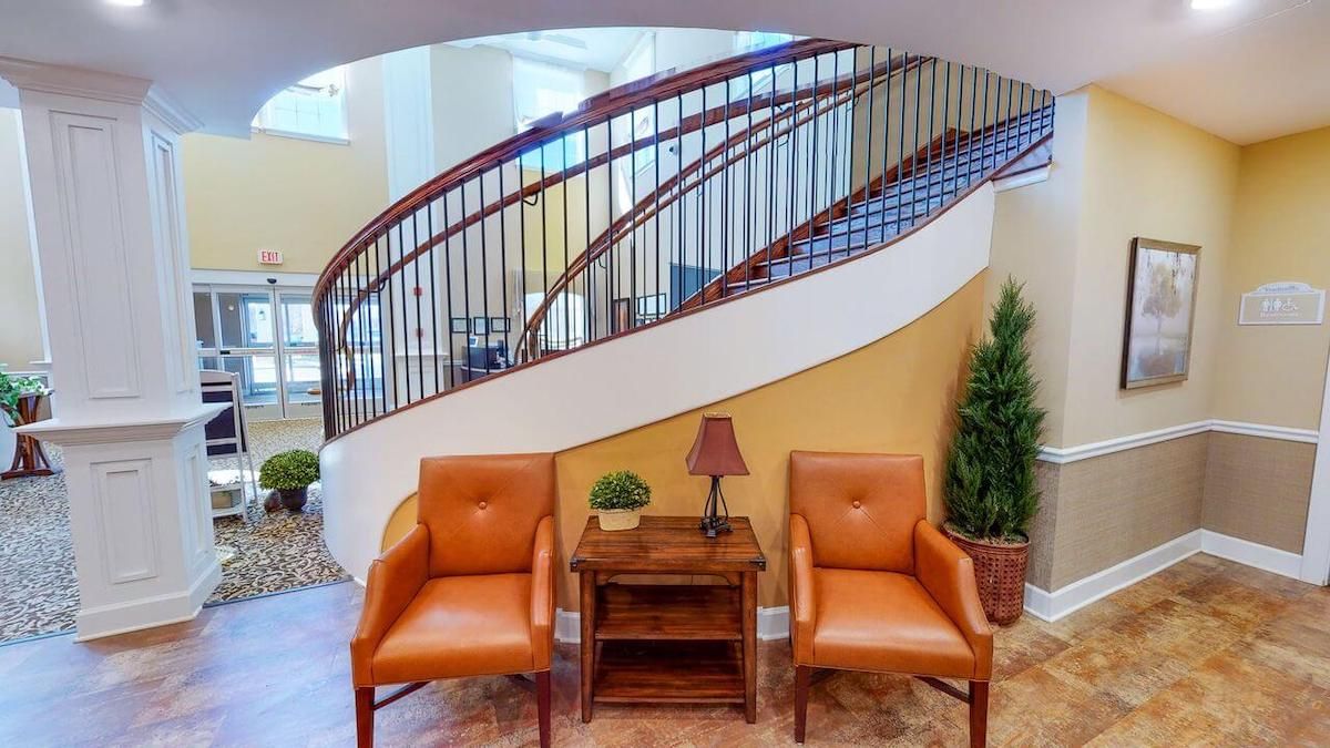 A cozy seating area with two orange chairs and a small table, positioned in front of a grand spiral staircase.