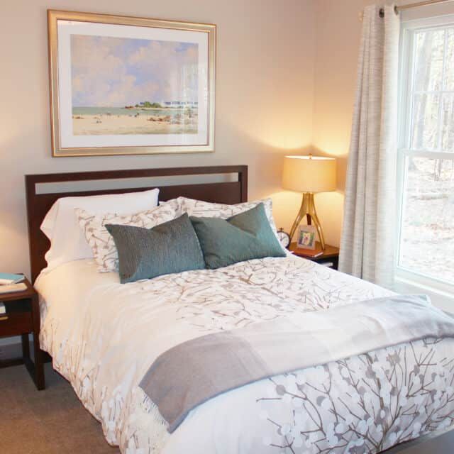A cozy bedroom with a well-made bed, decorative pillows, and a bedside lamp.