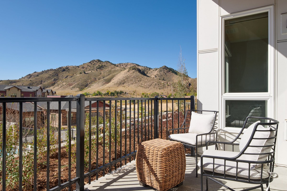 A scenic balcony with outdoor furniture overlooking mountains under a clear blue sky.