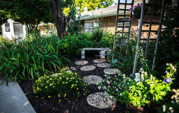 A tranquil garden with a stone pathway leading to a bench, surrounded by lush greenery and colorful flowers.