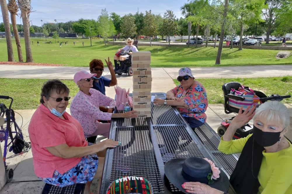 A group of elderly women enjoying a game of Jenga at a park picnic table on a sunny day.