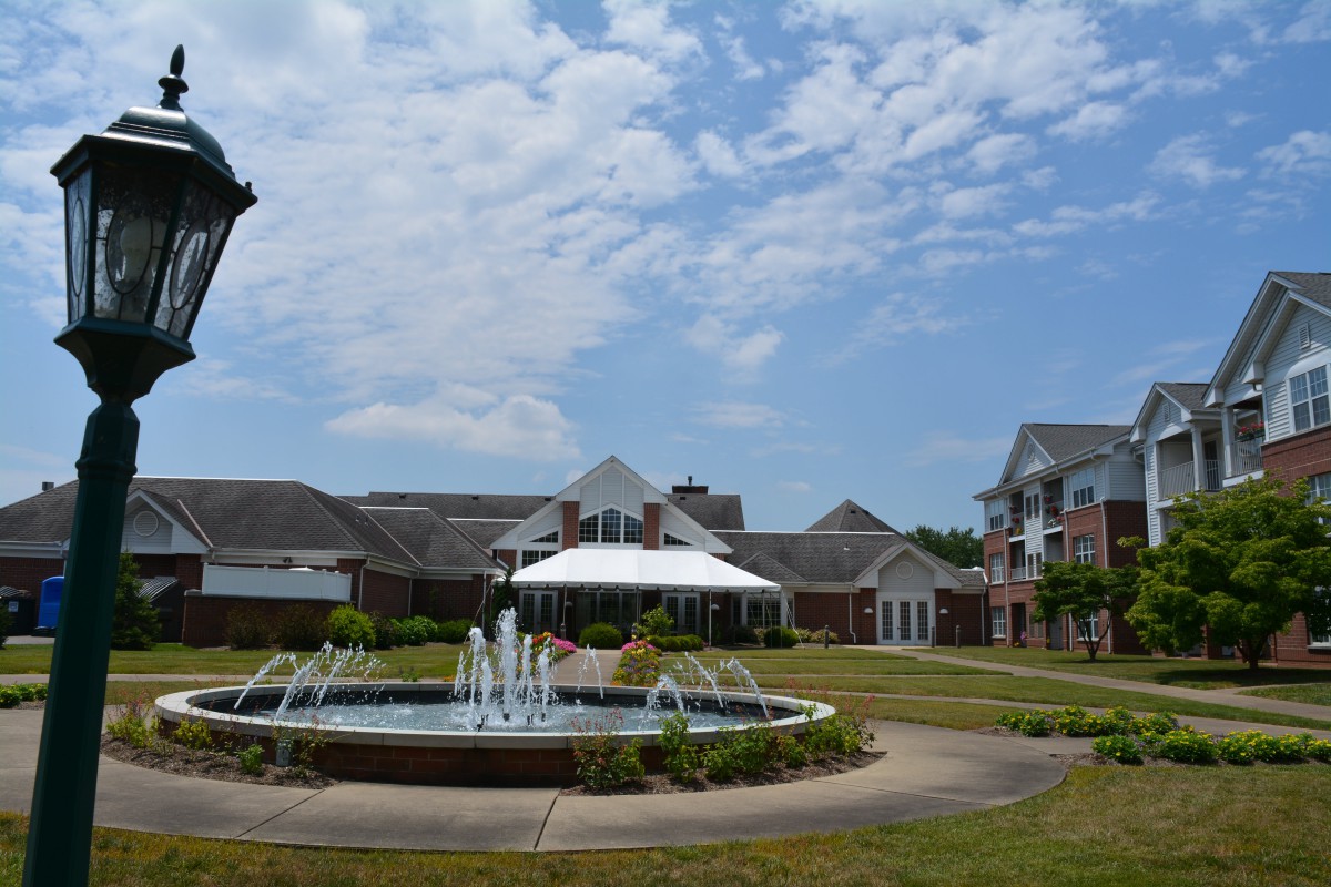 A scenic view of a building complex with a central fountain under a partly cloudy sky.