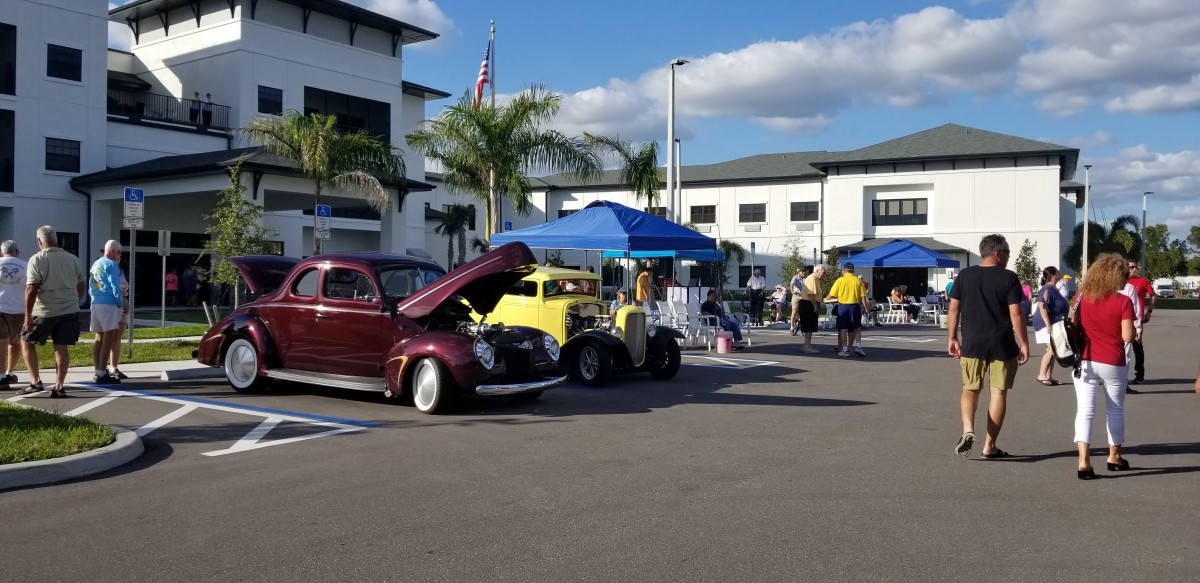 A car show featuring vintage vehicles on display under a sunny sky, with tents and people in the background.