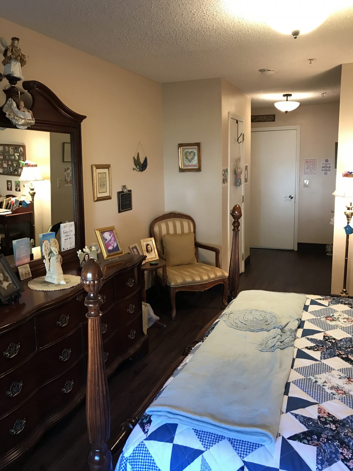 A cozy bedroom featuring a bed, a dresser with decorative items, and an upholstered chair.