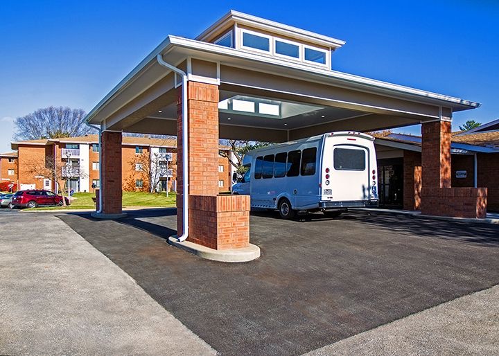 A white bus parked under a canopy in front of a brick building on a sunny day.