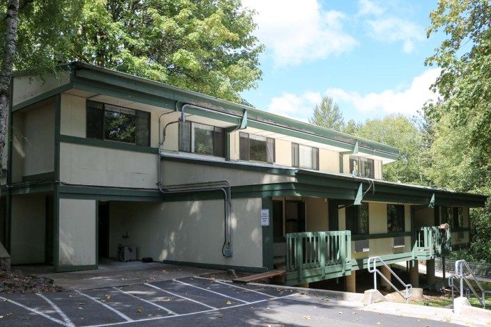 A two-story building surrounded by trees and a parking area.