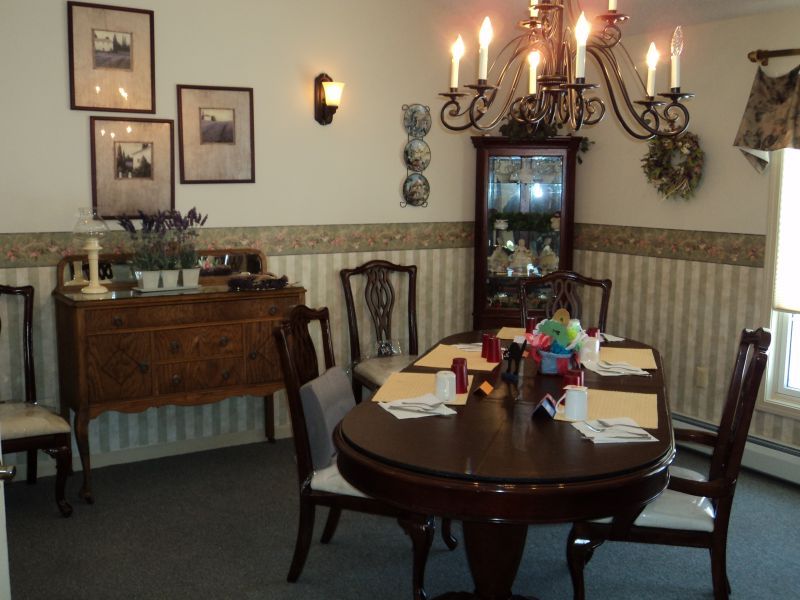 A cozy dining room with a set table, chandelier lighting, and classic wooden furniture.