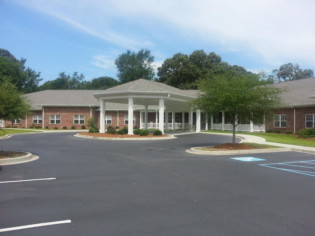A single-story building with a large parking lot and surrounding greenery under a clear sky.