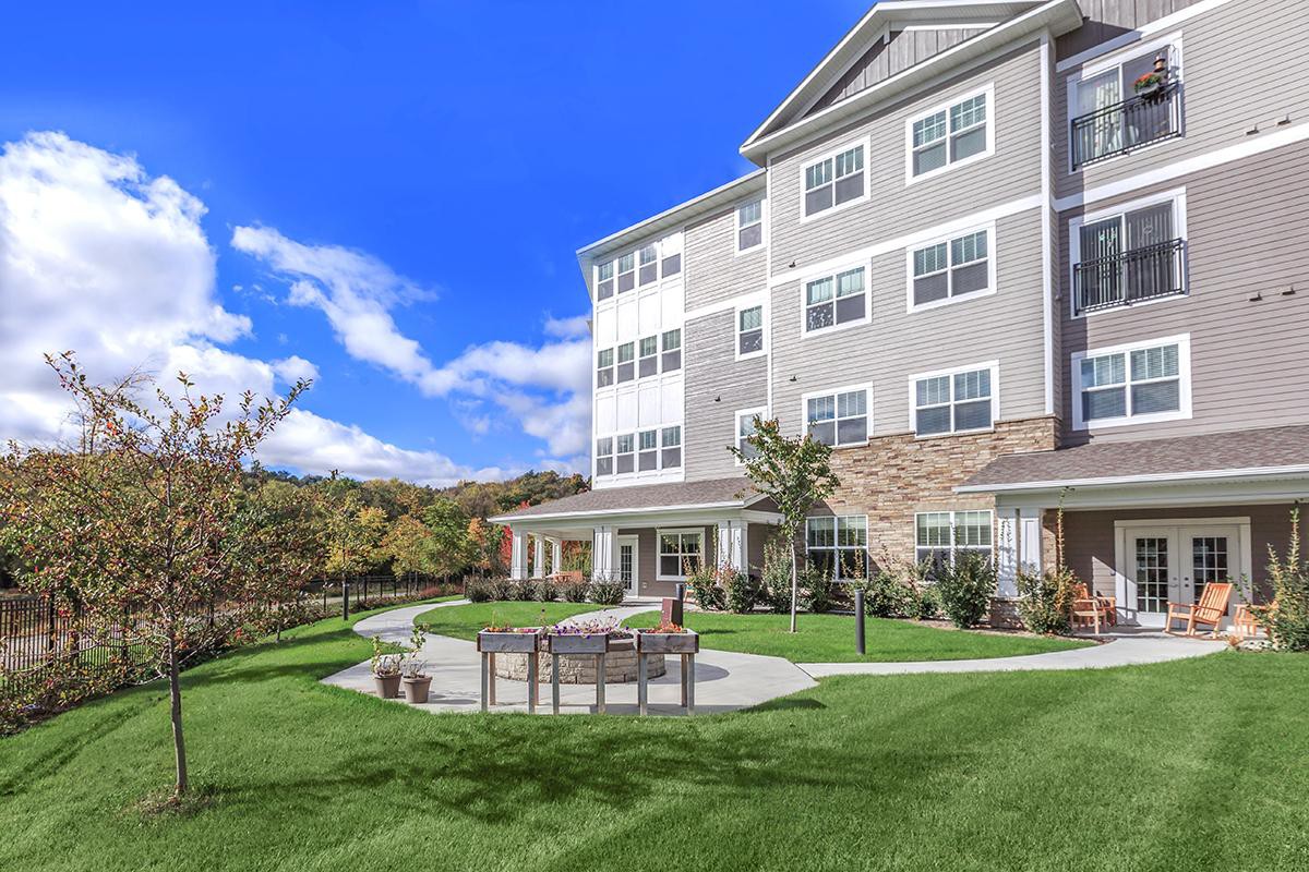 A modern apartment building with well-maintained landscaping and outdoor seating under a clear blue sky.