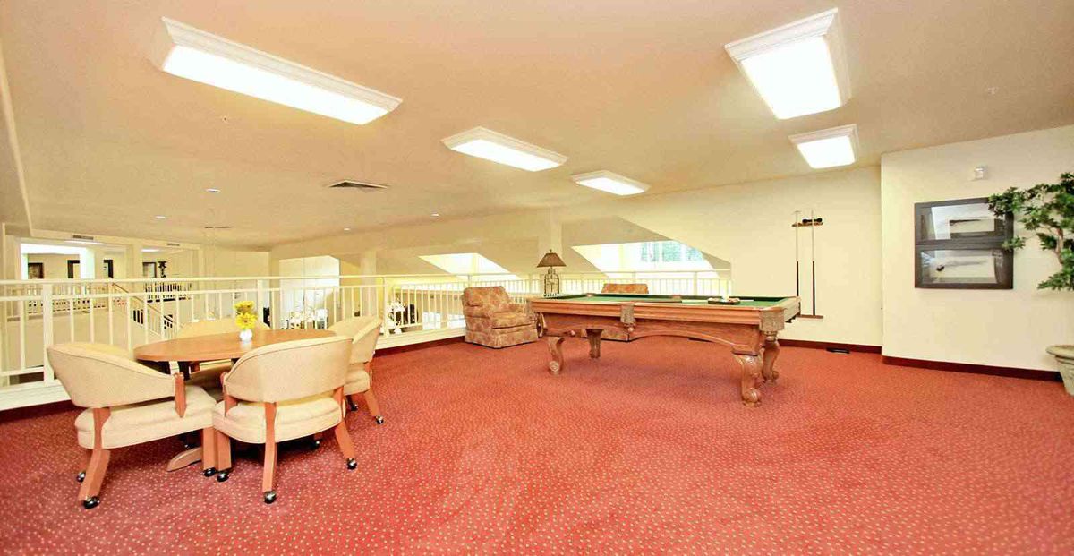 A spacious game room featuring a pool table and comfortable seating on a carpeted floor.