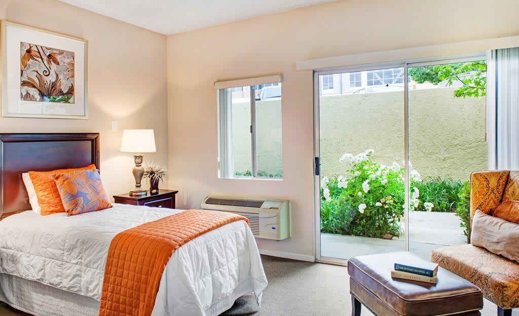 A cozy and modern bedroom with natural light, featuring a comfortable bed and a window view of greenery.