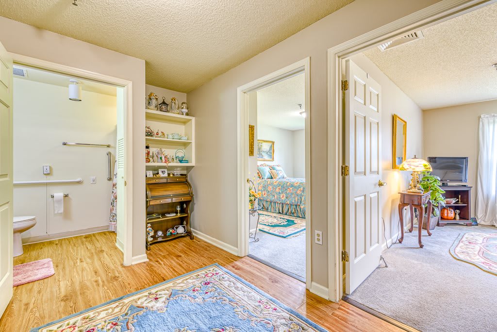 A cozy hallway with open doorways leading to carpeted rooms, featuring a decorative rug and neatly arranged shelves.