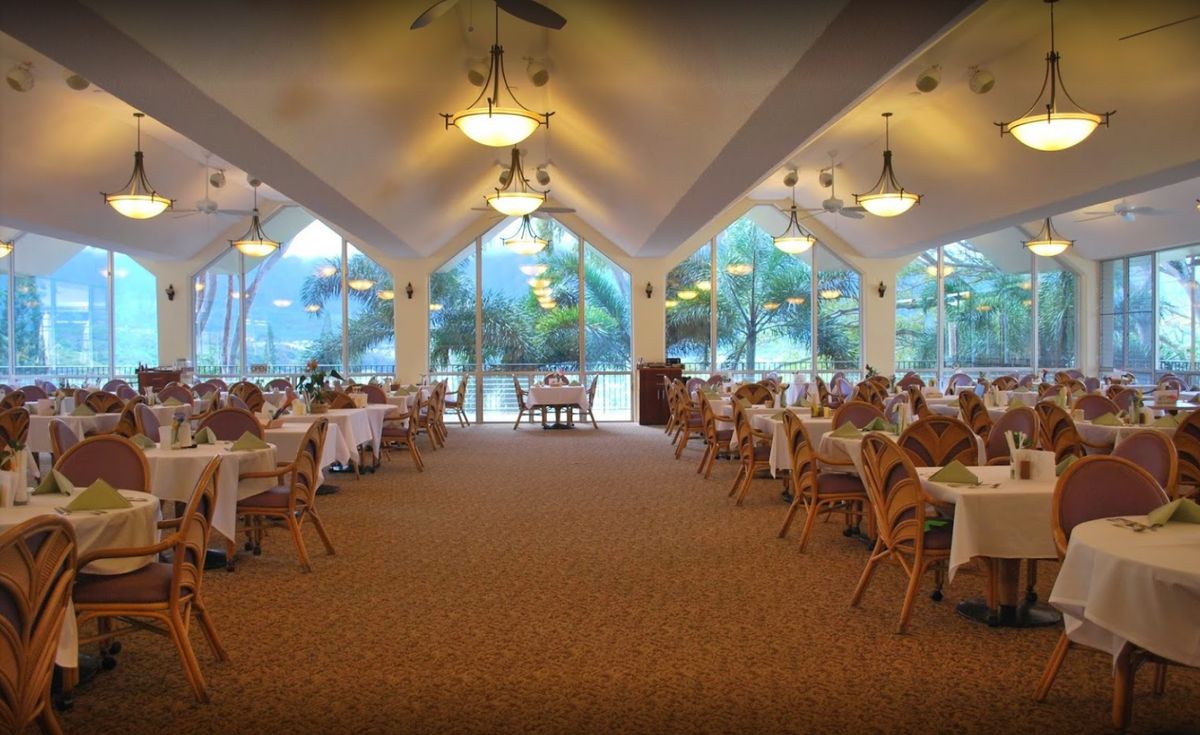 A spacious restaurant interior with neatly arranged tables and chairs, illuminated by elegant lighting fixtures and large windows offering a scenic view.