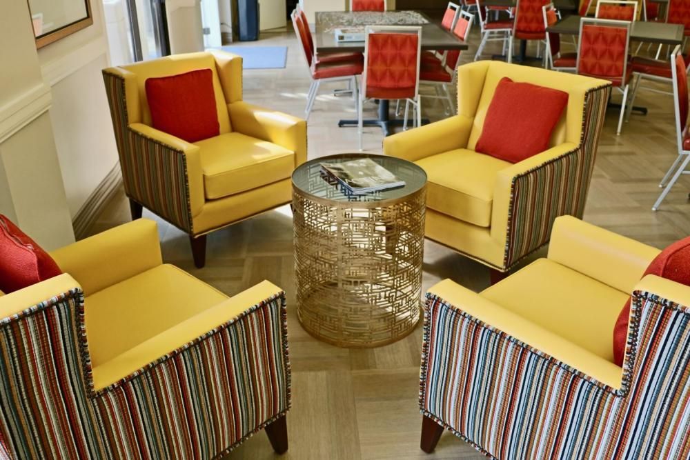 A vibrant seating area featuring yellow chairs with red pillows and a glass table.