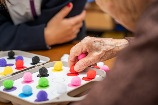 An elderly person engaging in a colorful cognitive game, focusing on sorting small pom-poms.