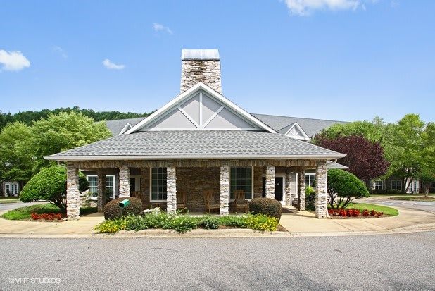 A well-maintained house with stone exterior and a chimney, surrounded by landscaped greenery.