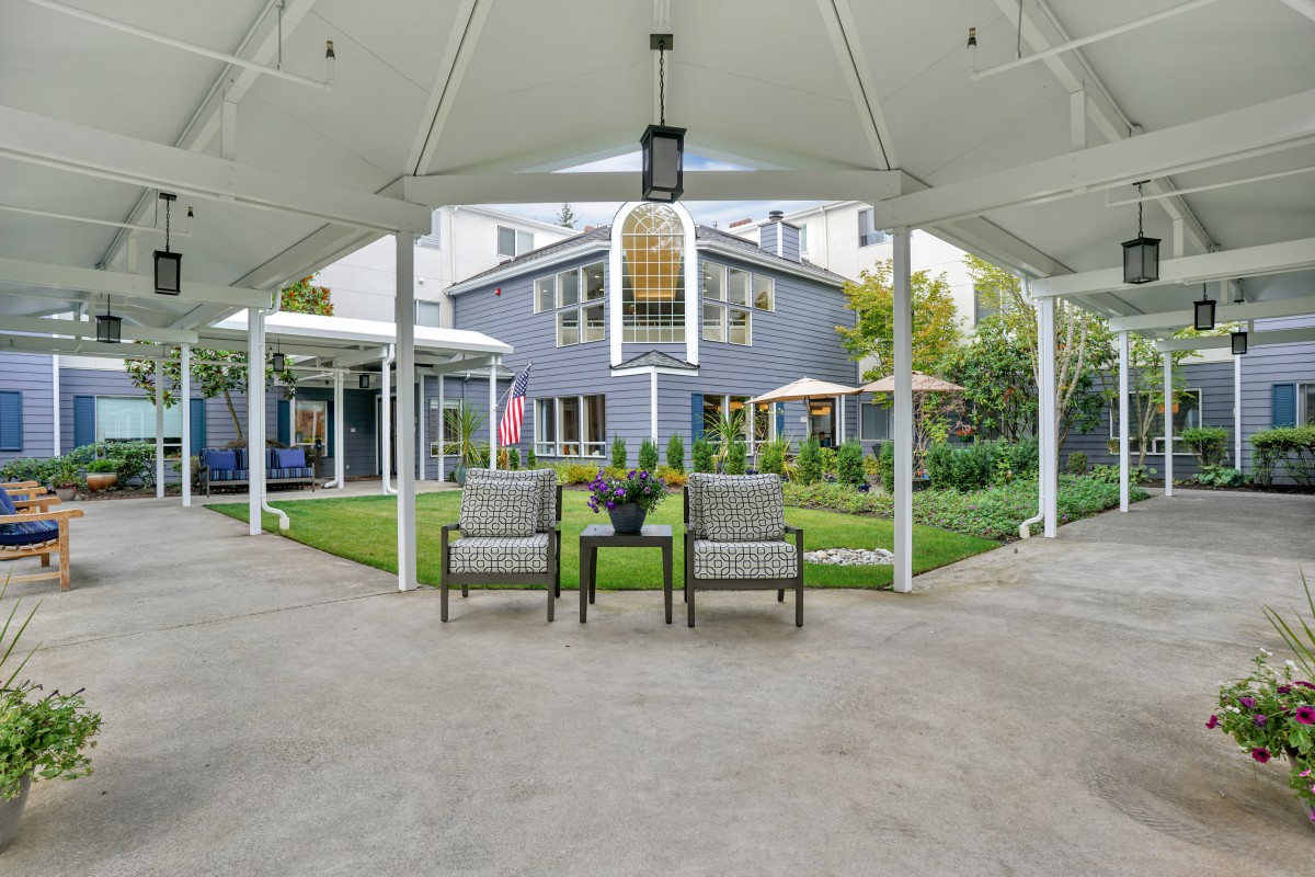A view of a modern house with a spacious backyard patio, featuring lawn chairs and a well-maintained garden.