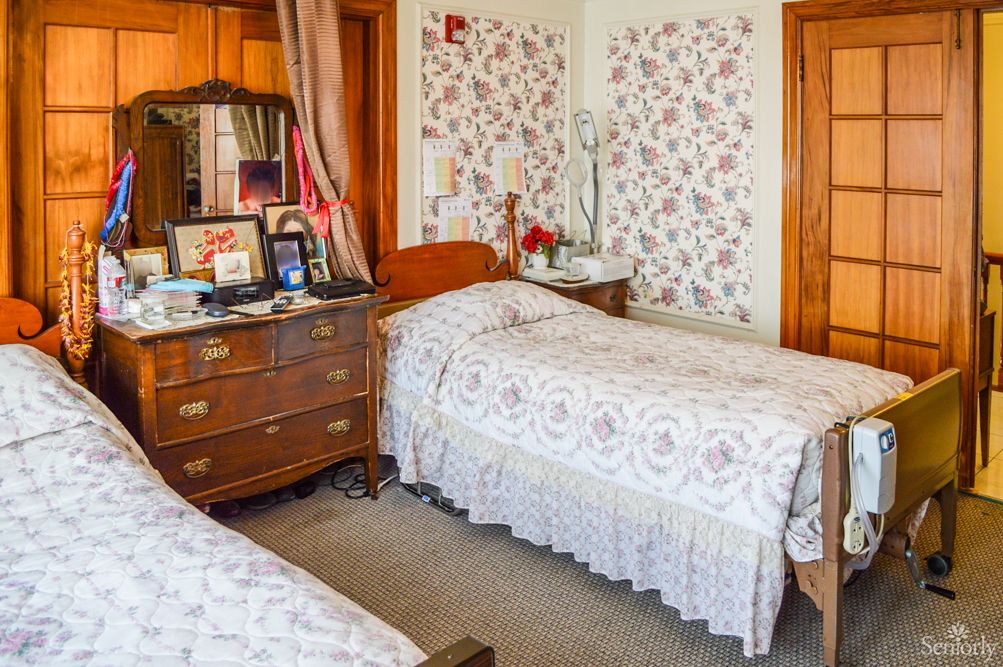 A vintage-style bedroom with twin beds, floral wallpaper, and an antique dresser with a mirror.