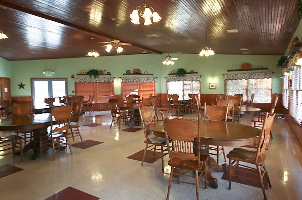 A cozy dining area featuring wooden tables and chairs, with warm lighting and a spacious layout.