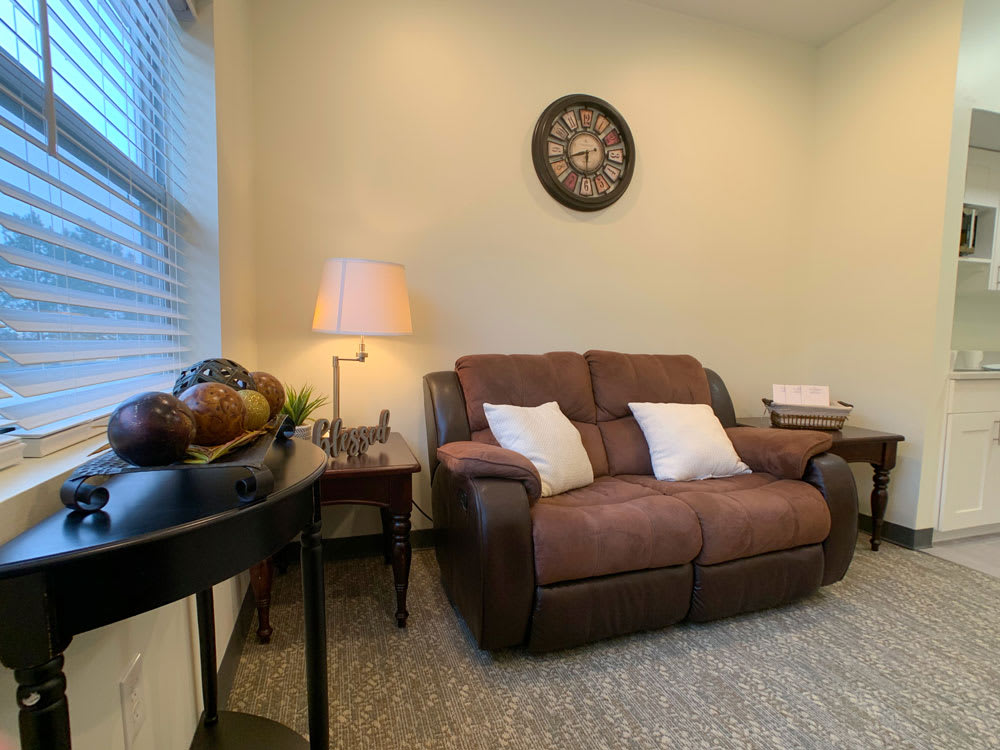 A cozy living room space with a brown sofa, accent pillows, a floor lamp, and a wall clock.
