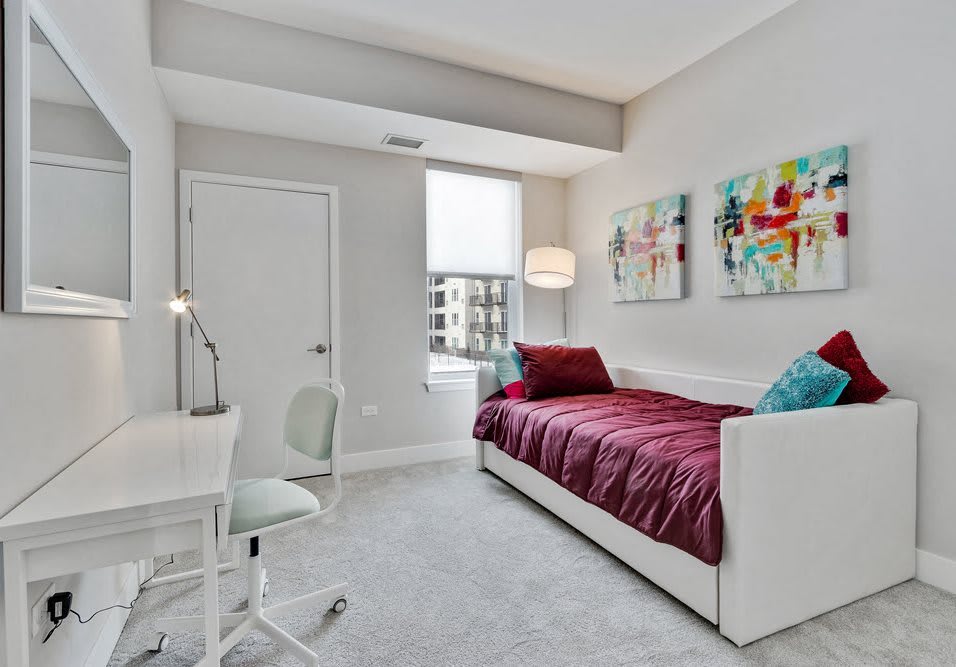 A modern minimalist bedroom with a single bed, desk, and colorful artwork.