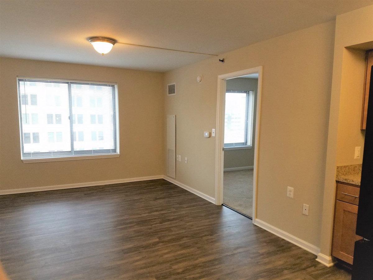 An empty room with hardwood flooring, a window, and a doorway leading to another room.