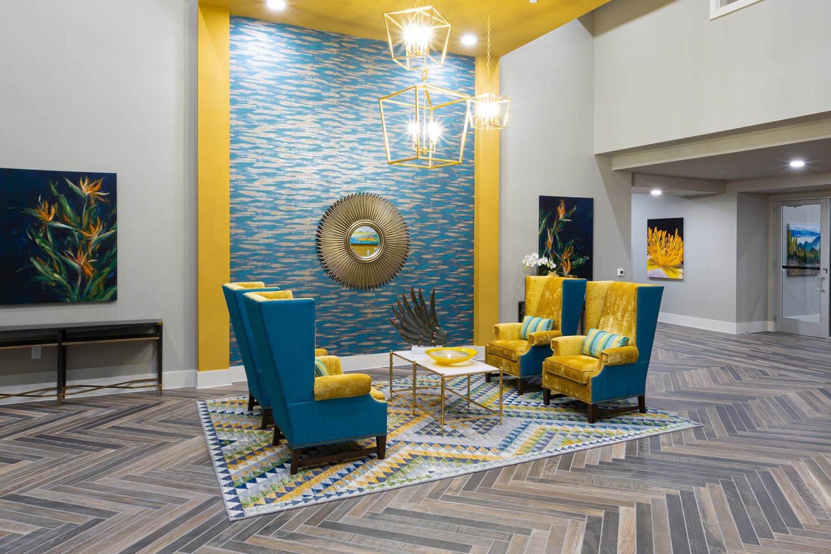 A modern living room with a vibrant blue and yellow color scheme, featuring stylish wingback chairs, a geometric rug, and contemporary lighting.