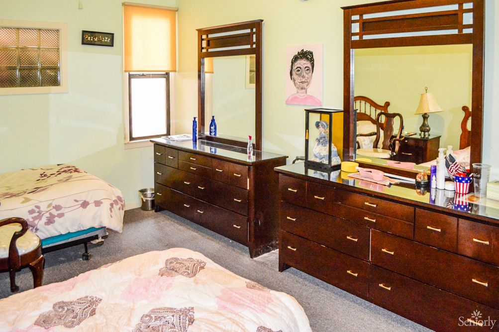 A cozy bedroom featuring wooden dressers with mirrors and a neatly made bed.