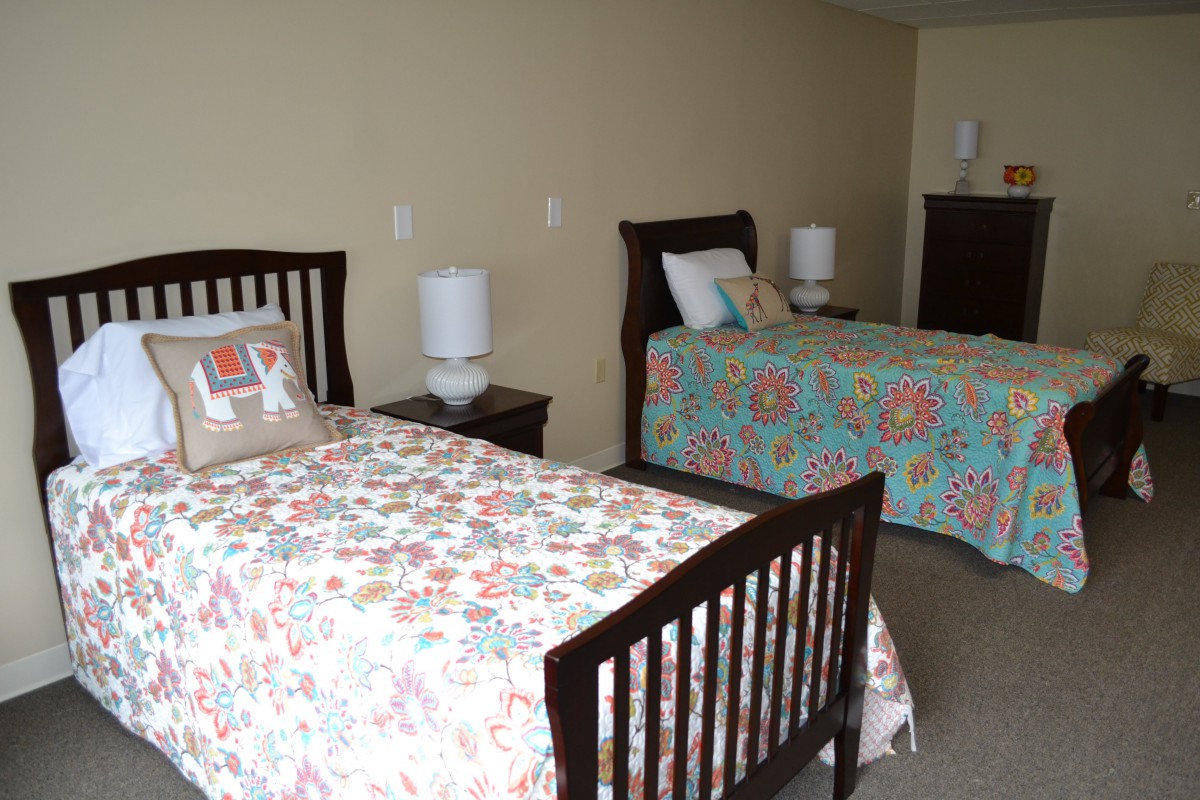 A tidy bedroom with two beds, each adorned with colorful floral bedspreads, alongside nightstands and lamps.