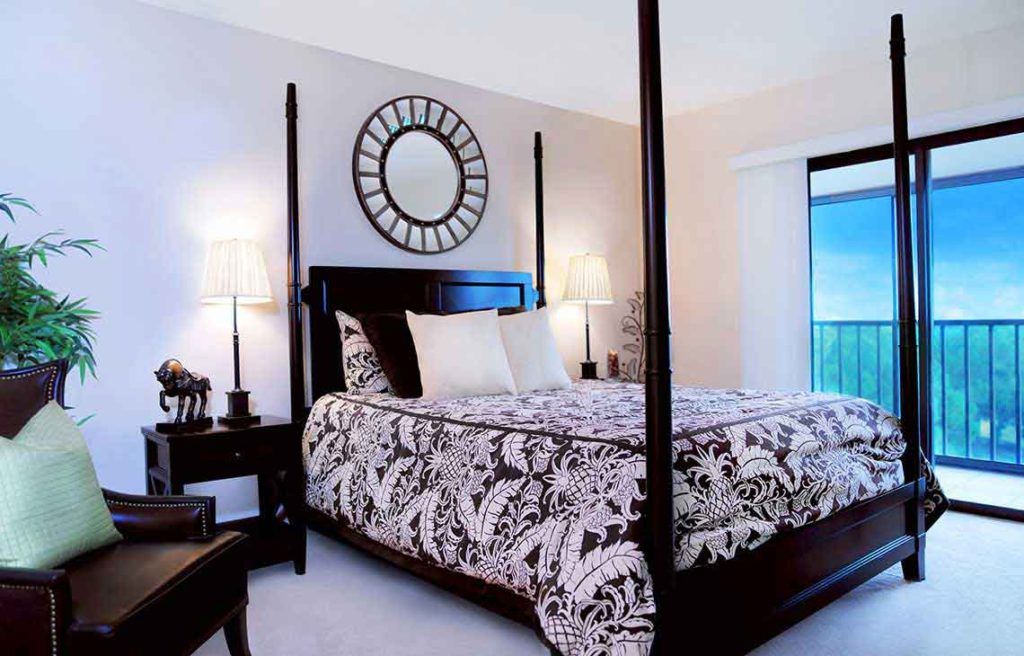 A stylish bedroom featuring a four-poster bed with patterned bedding, complemented by a decorative mirror and elegant nightstands.