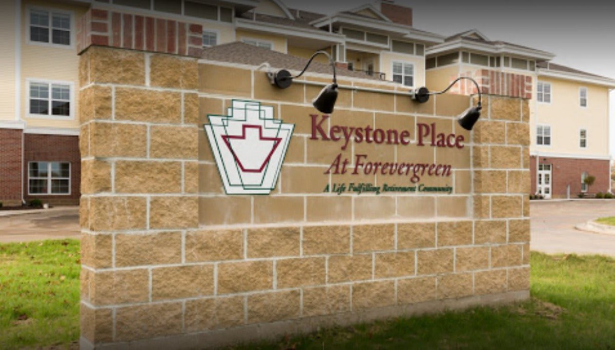 A sign for Keystone Place at Forevergreen, a senior living community, mounted on a stone wall outside a building.
