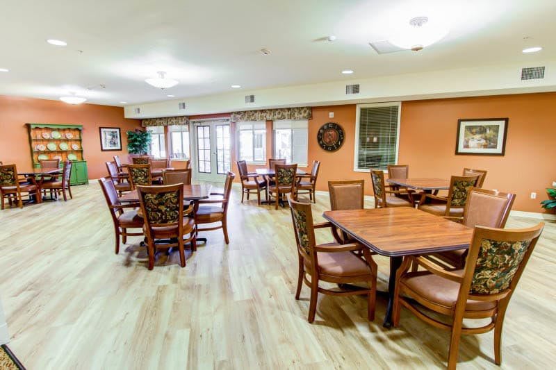 A spacious dining area with multiple tables and wooden chairs, featuring bright lighting and a warm atmosphere.