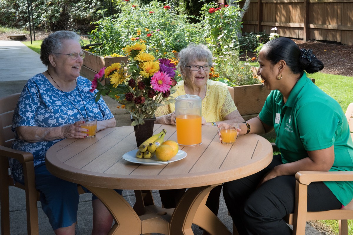 A group of people enjoying a pleasant conversation outdoors in a garden setting with flowers and drinks on the table.
