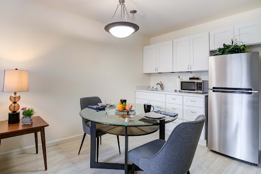 A modern kitchen and dining area featuring a glass-top table and stylish gray chairs, complemented by sleek white cabinetry.