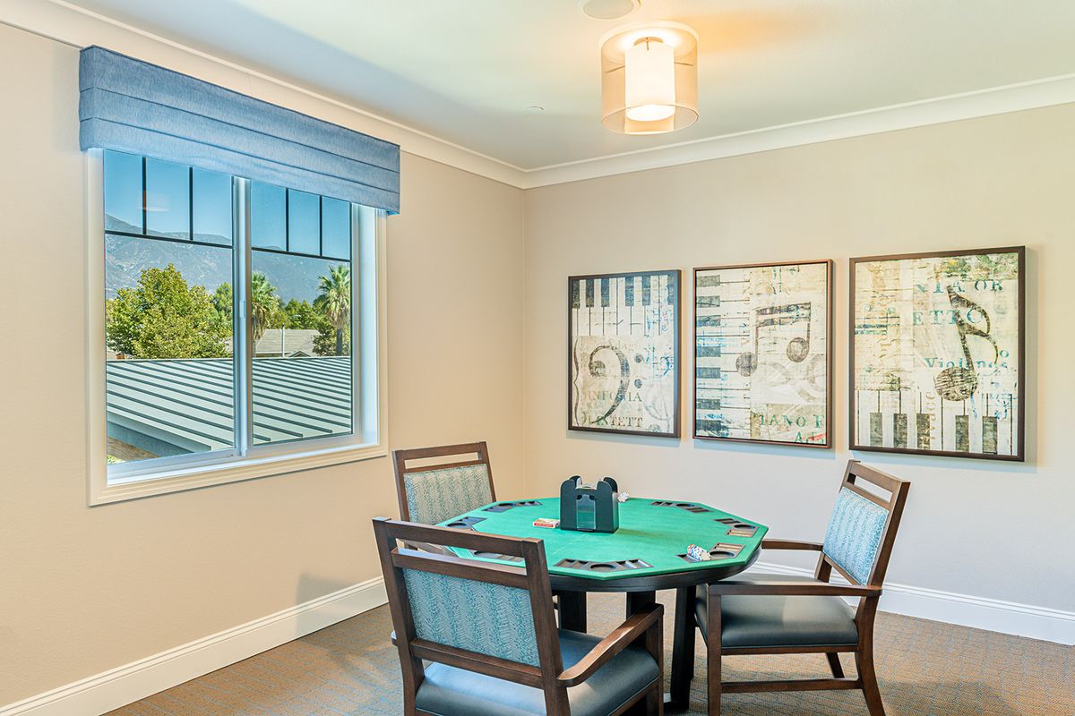 A cozy game room featuring a poker table surrounded by chairs, with artwork on the walls and natural light from the window.