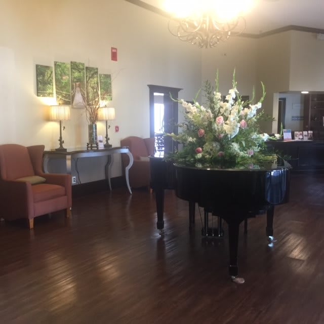 A spacious lobby with a grand piano adorned with flowers, featuring elegant decor and comfortable seating.