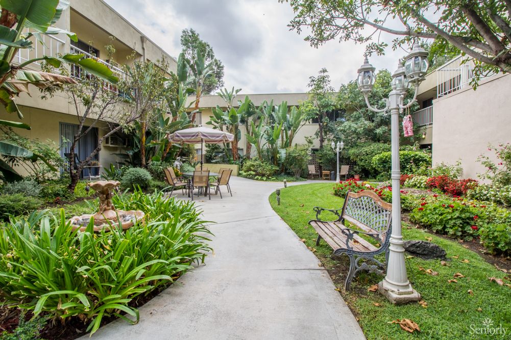 A serene garden pathway with benches, surrounded by lush greenery and outdoor seating.