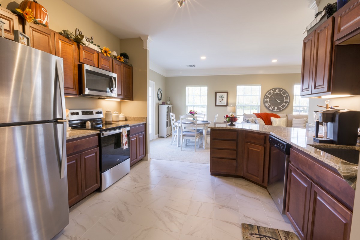 A modern kitchen with wood cabinets and stainless steel appliances, featuring an open layout leading to a dining area.
