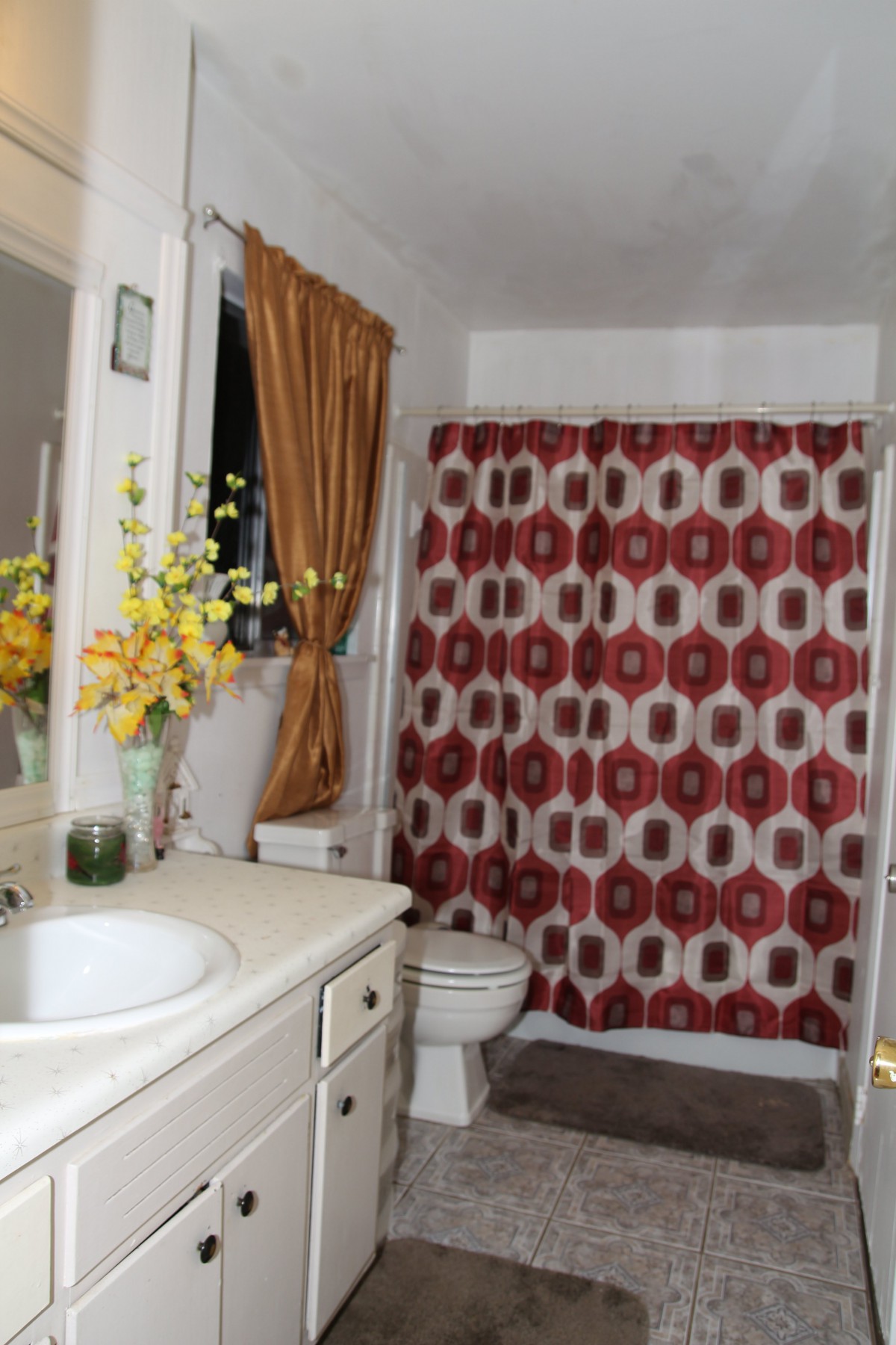 A bathroom with a red and white geometric shower curtain, sink, and decorative flowers.