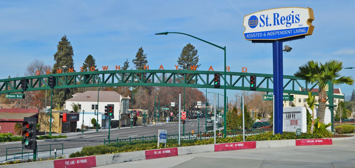 A city entrance sign spanning across a street with trees and buildings in the background.