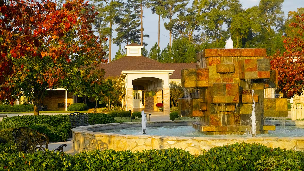 A scenic outdoor view featuring a fountain in front of a building surrounded by lush greenery and trees.
