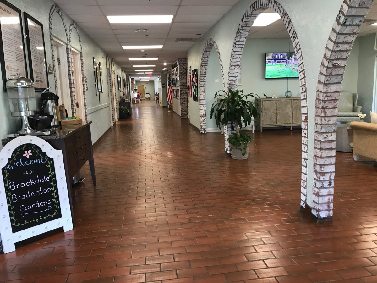 A spacious hallway with wooden floors and brick archways, featuring plants and a wall-mounted television.