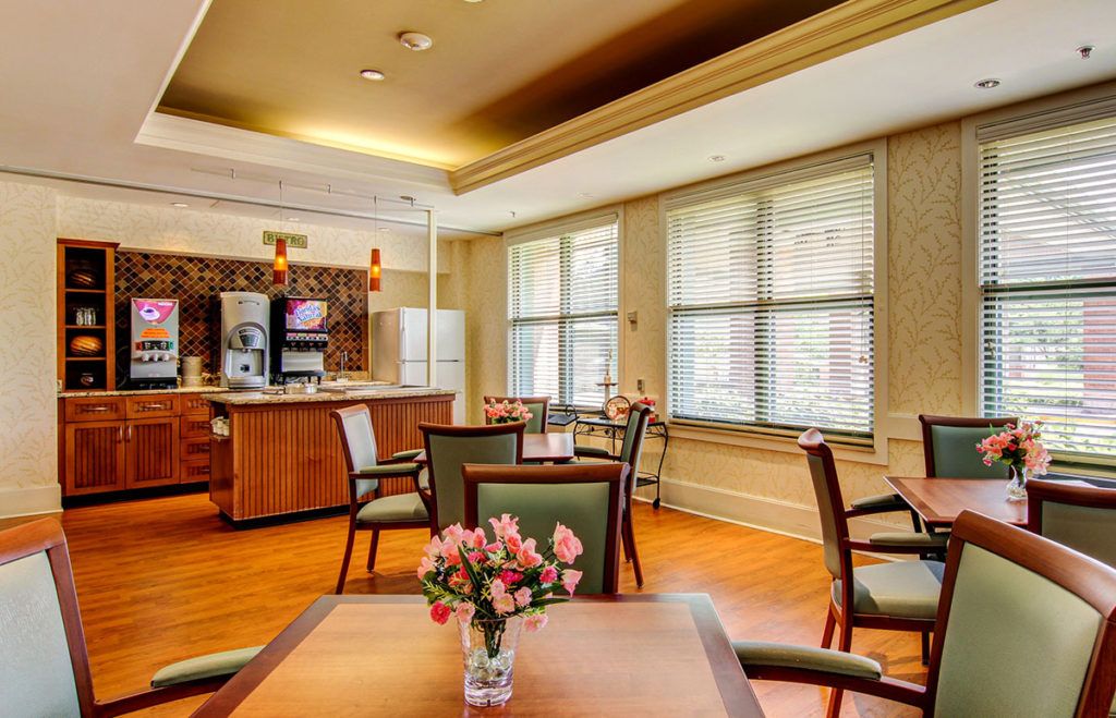A modern dining area with a kitchen in the background, featuring wooden furniture and decorative flowers on the table.