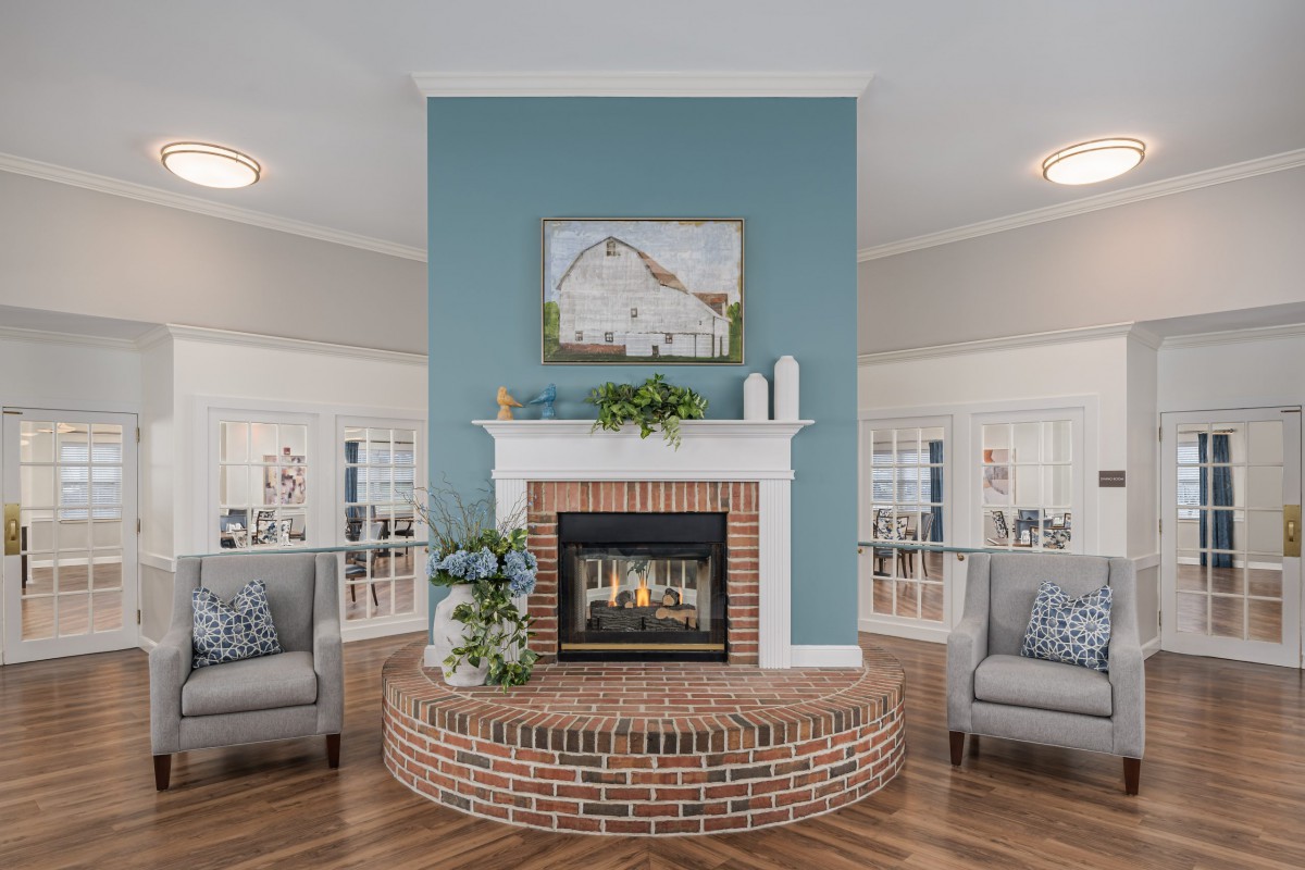 A cozy living room with a brick fireplace and blue accent wall, flanked by comfortable armchairs and elegant decor.