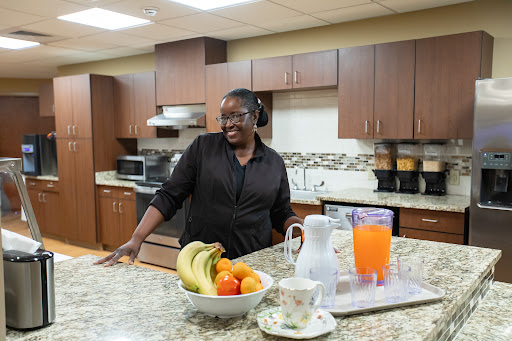 A cheerful woman enjoying her time in a well-equipped kitchen, surrounded by fresh fruits and beverages.