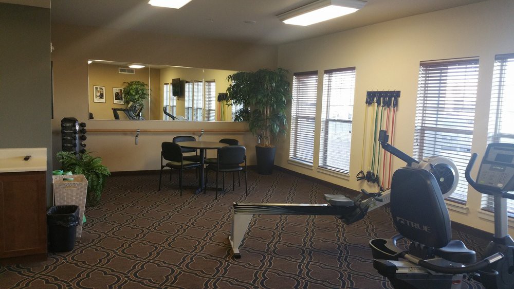 A small gym room featuring exercise equipment, mirrors, and natural lighting.