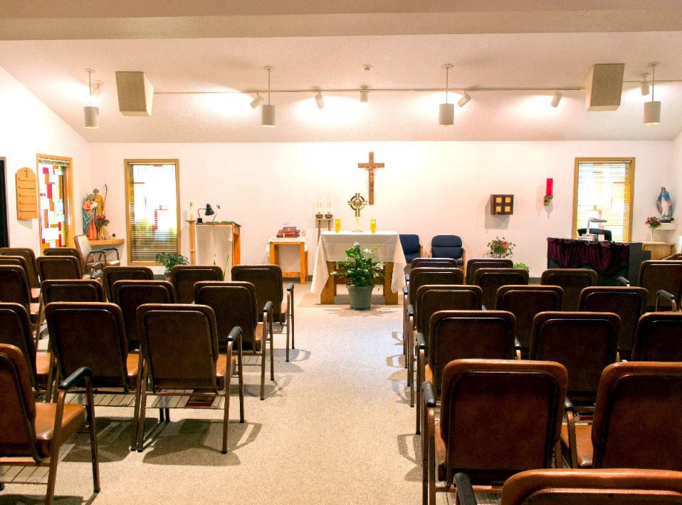 A small chapel interior with rows of seats facing an altar and a cross.