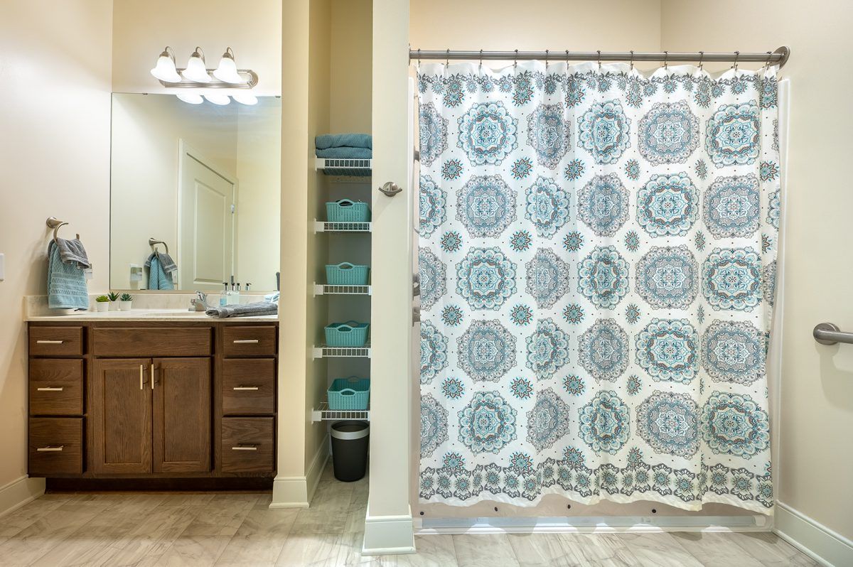 A neatly organized bathroom with a stylish patterned shower curtain and blue towels on shelves.