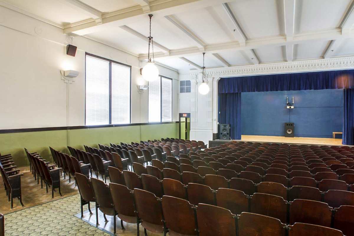 An empty auditorium with rows of seating facing a stage under soft lighting.